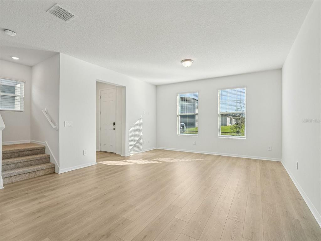 An empty living room features light wood-look flooring, white walls, and stairs on the left — 4685 CROSS PRAIRIE PARKWAY, ST CLOUD, FL