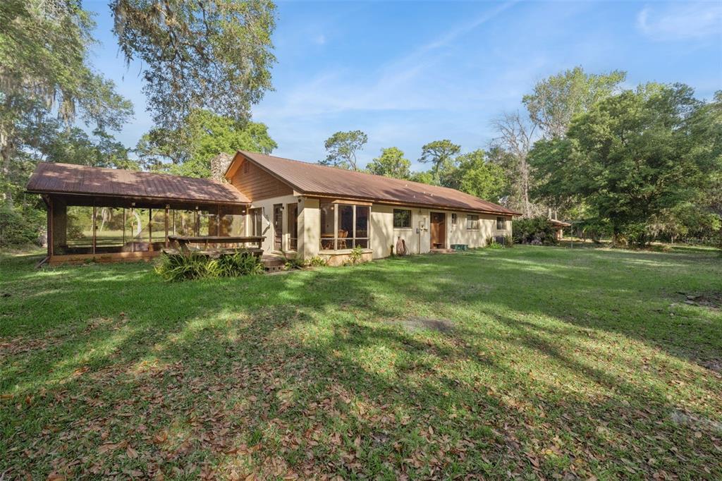 A single-story house with a metal roof and a large screened-in porch sits on grass — 2260 PANORAMA DRIVE, CHULUOTA, FL