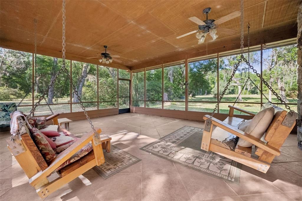 A screened-in porch features two wooden hanging swings, ceiling fans, and tile flooring — 2260 PANORAMA DRIVE, CHULUOTA, FL