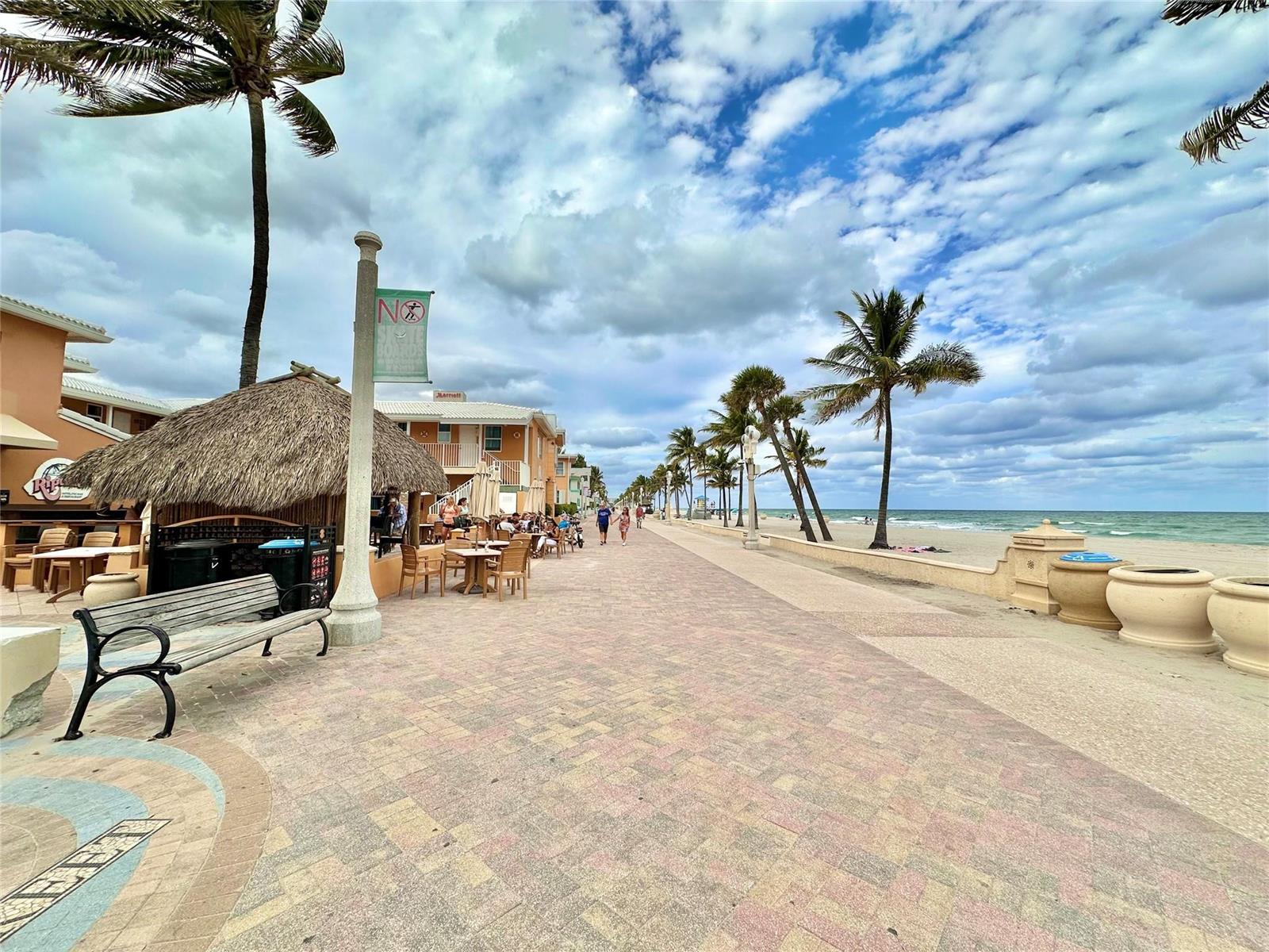 A paved boardwalk runs alongside a sandy beach with palm trees and outdoor restaurant seating — 2212 N Surf Road, Hollywood FL 33019, HOLLYWOOD, FL