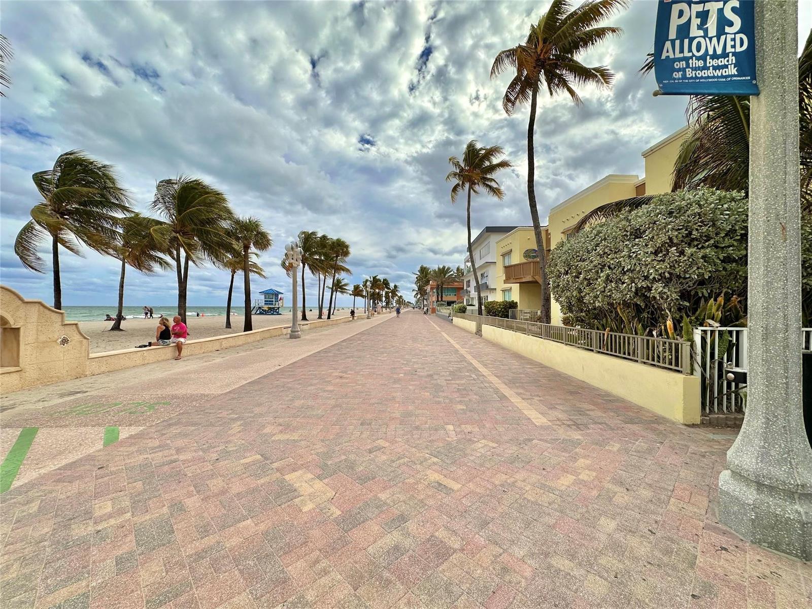 A paved boardwalk stretches along a beach with palm trees and buildings under a cloudy sky — 2212 N Surf Road, Hollywood FL 33019, HOLLYWOOD, FL