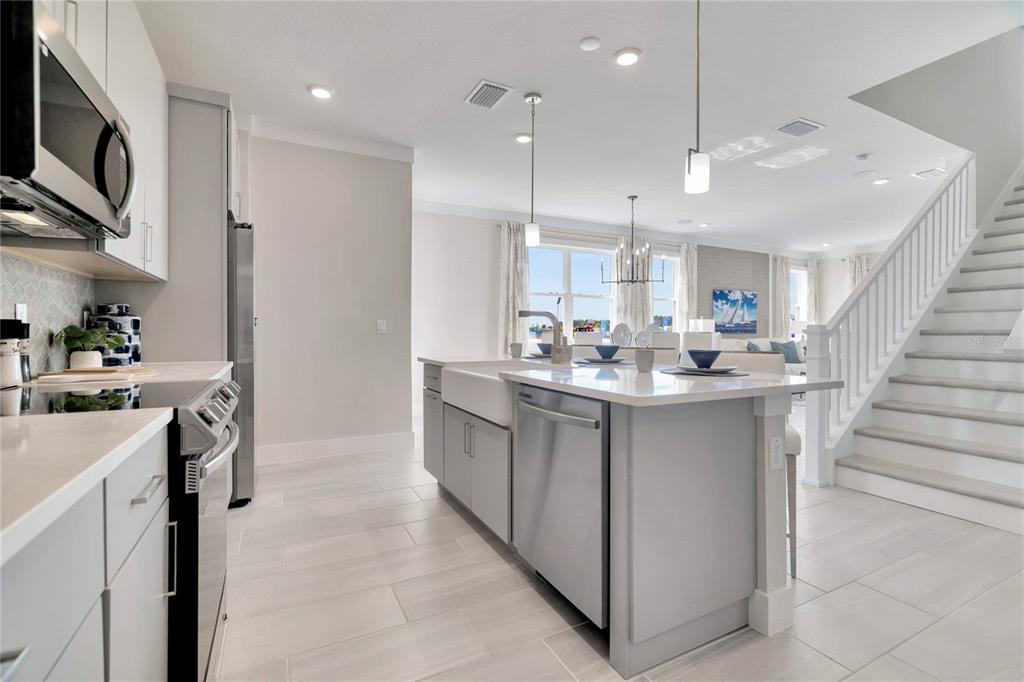 A modern kitchen with a large island, white cabinetry, and a staircase to the right — 32119 ANCHOR POINT DRIVE, WESLEY CHAPEL, FL