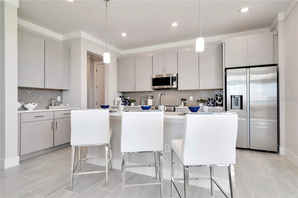 A modern kitchen features light gray cabinetry, stainless steel appliances, and a white breakfast bar — 32119 ANCHOR POINT DRIVE, WESLEY CHAPEL, FL
