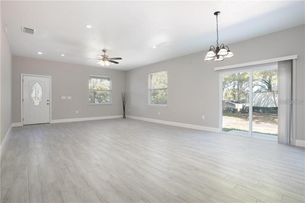 A spacious living room with light gray walls, wood-look tile flooring, and a sliding glass door — 1777 BURROWS LANE, SANFORD, FL