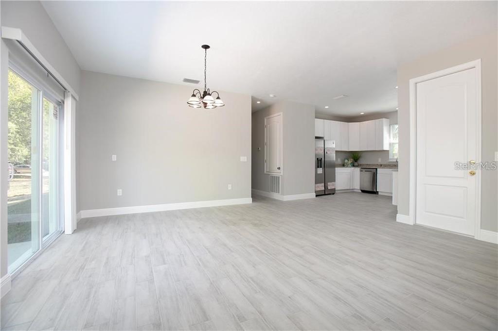 An open-concept dining area with light wood-look tile flooring leads into a white kitchen — 1777 BURROWS LANE, SANFORD, FL