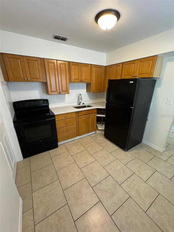 A kitchen features wood cabinets, a black stove, a black refrigerator, and tiled flooring — 2027 37TH STREET S, ST PETERSBURG, FL