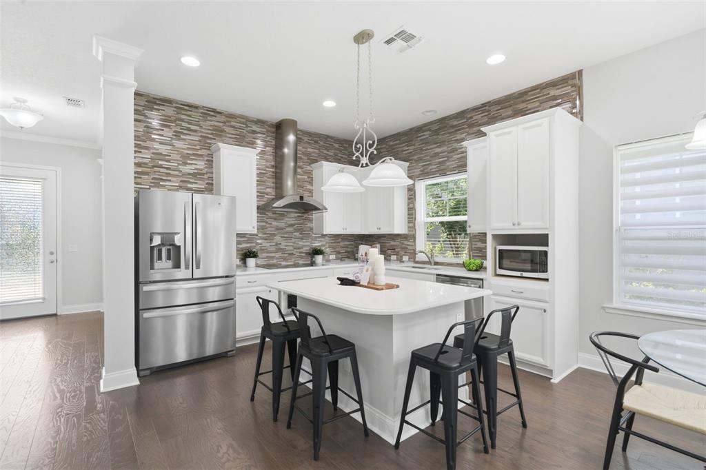 A modern kitchen features white cabinetry, stainless steel appliances, a center island, and stone backsplash — 13856 ELIOT AVENUE, ORLANDO, FL