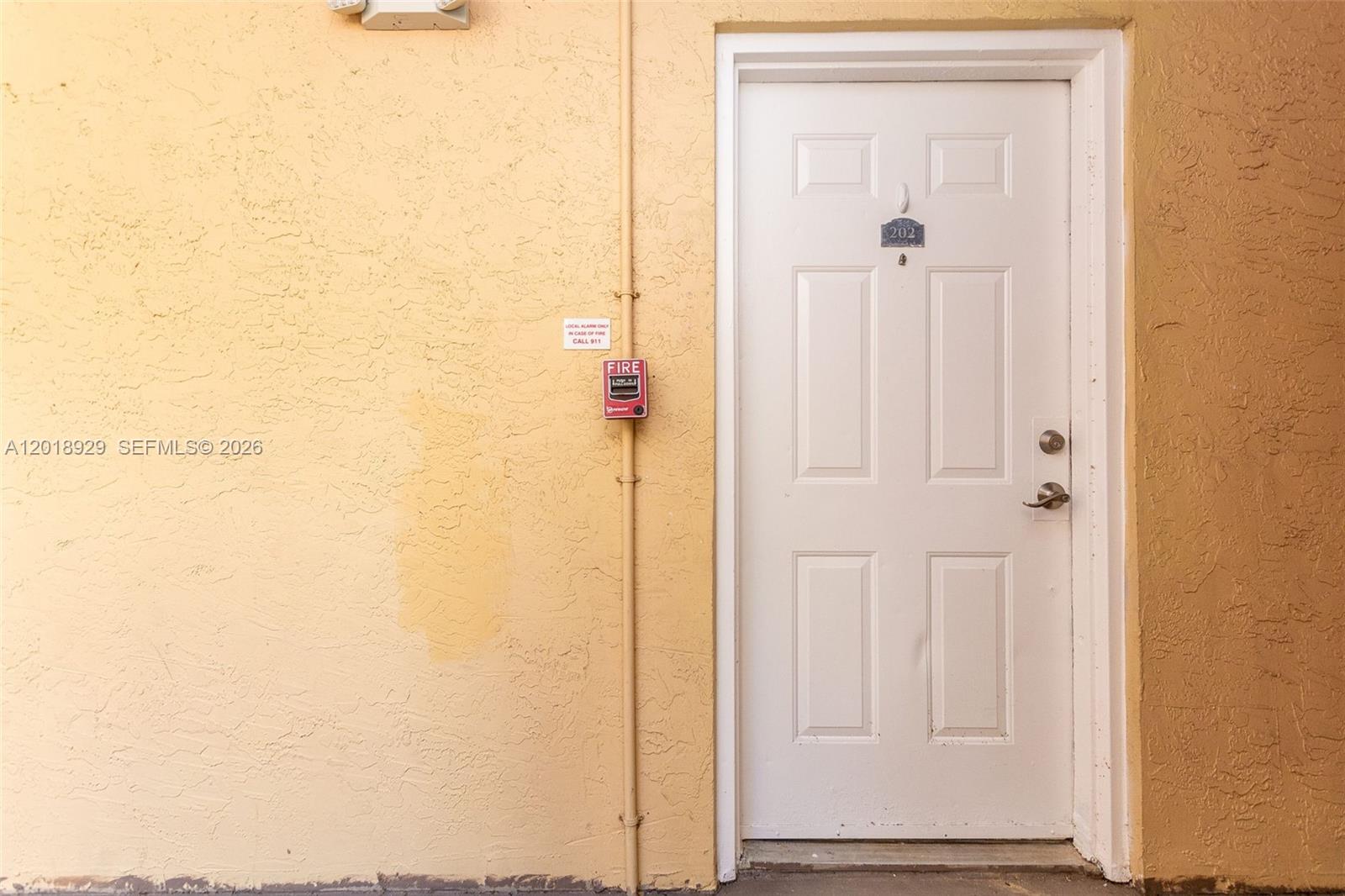 A white door labeled 202 is set into a textured, light yellow exterior wall — 5721 Riverside Dr, Coral Springs FL 33067, CORAL SPRINGS, FL
