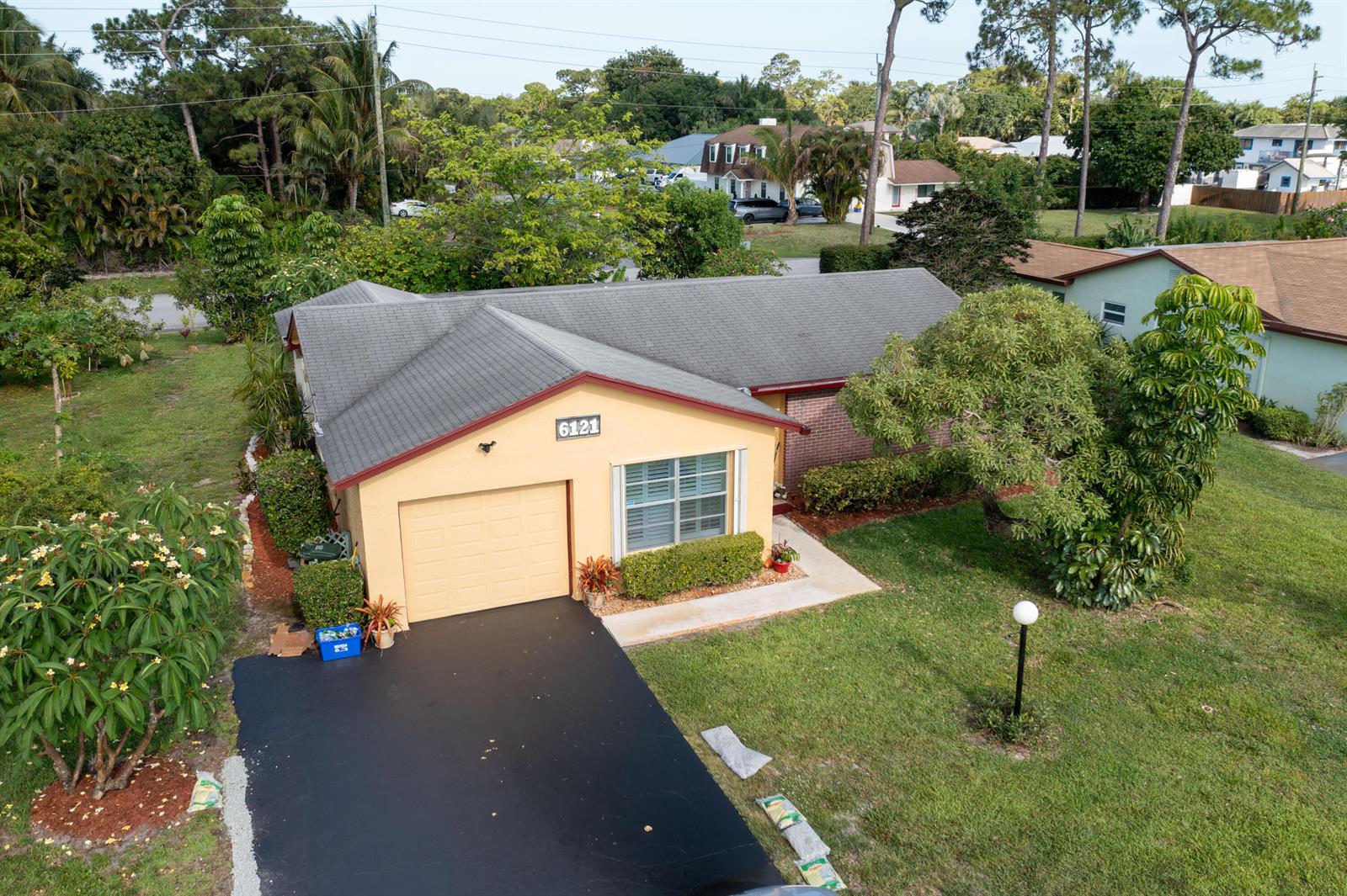 An aerial view shows a single-story house with a yellow facade, garage, and asphalt driveway — 6121 Rainbow Circle, FL 33463, FL