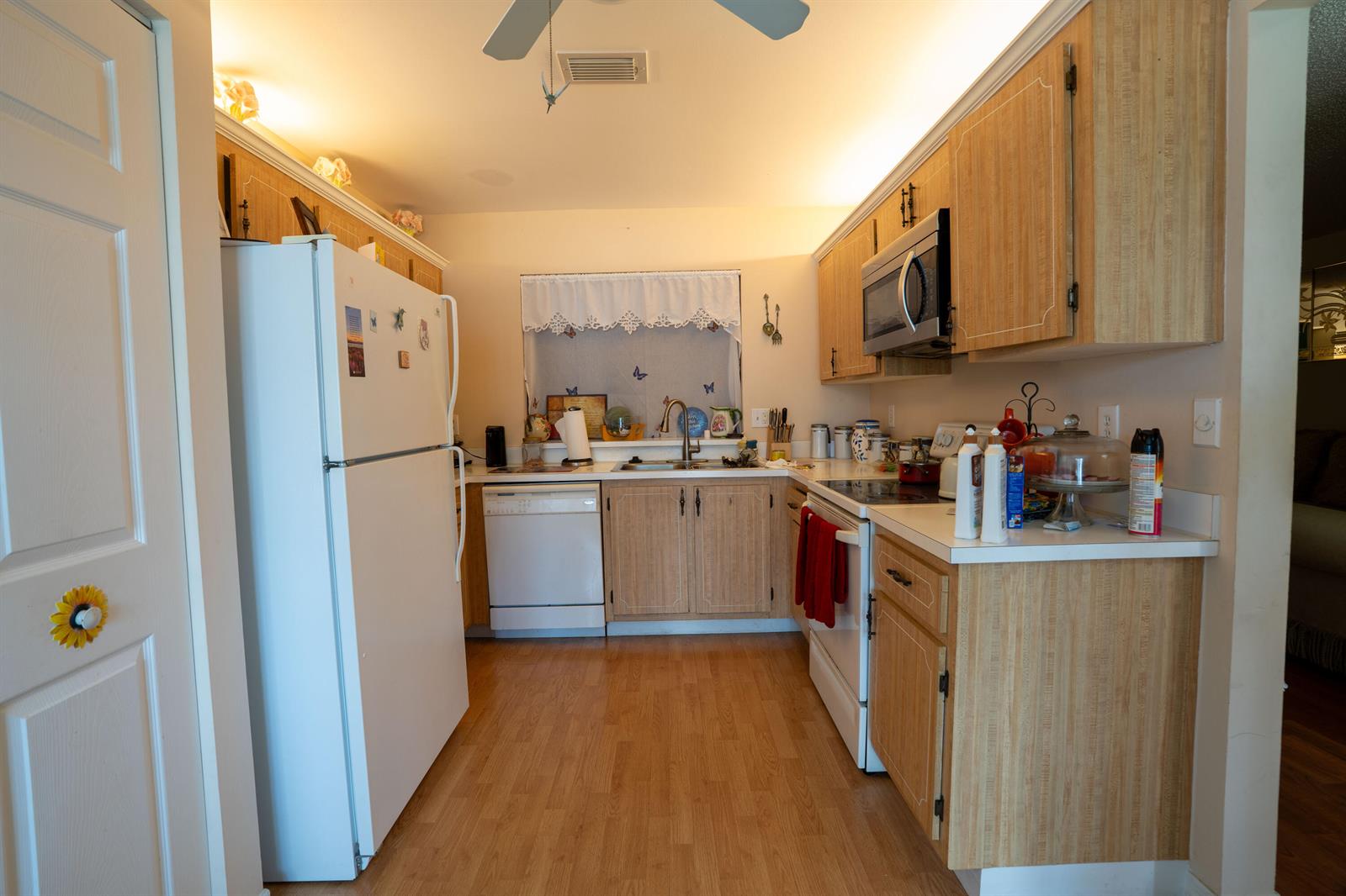 A kitchen features light wood cabinets, white appliances, a window above the sink, and laminate flooring — 6121 Rainbow Circle, FL 33463, FL