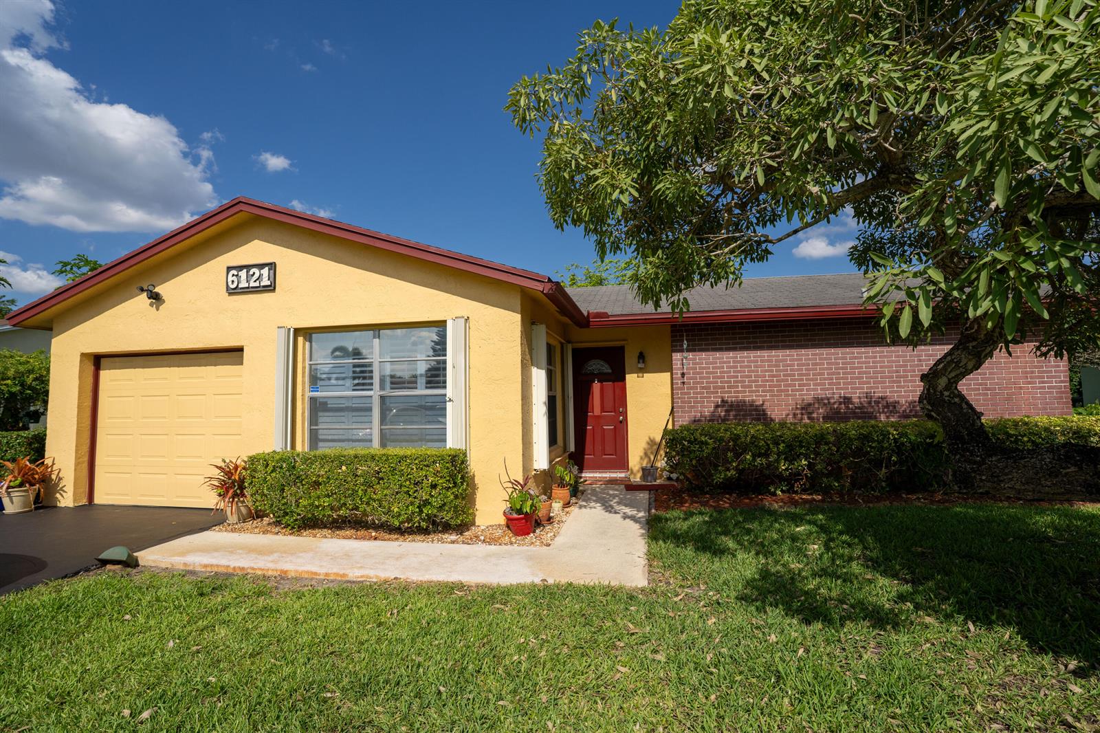 A yellow house with a brick facade, a garage, and a large tree in the yard — 6121 Rainbow Circle, FL 33463, FL