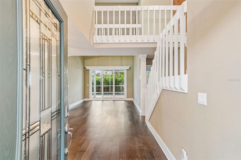 An entryway with hardwood floors, a white staircase railing, and a view of a pool — 1128 MAINSAIL DRIVE, TARPON SPRINGS, FL