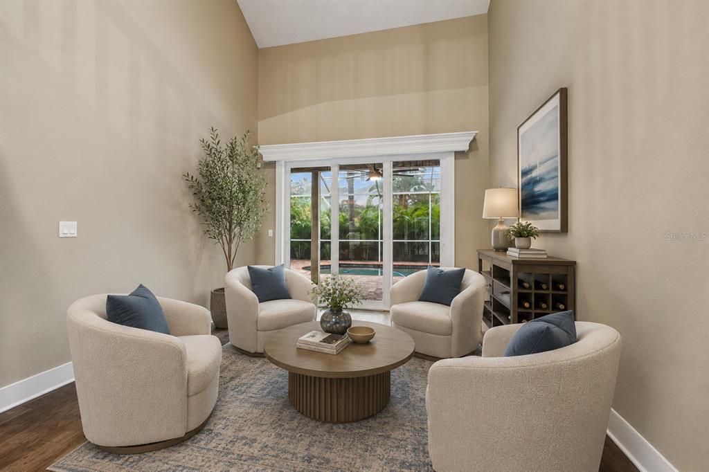 A living room with four cream-colored armchairs, a round coffee table, and sliding glass doors — 1128 MAINSAIL DRIVE, TARPON SPRINGS, FL