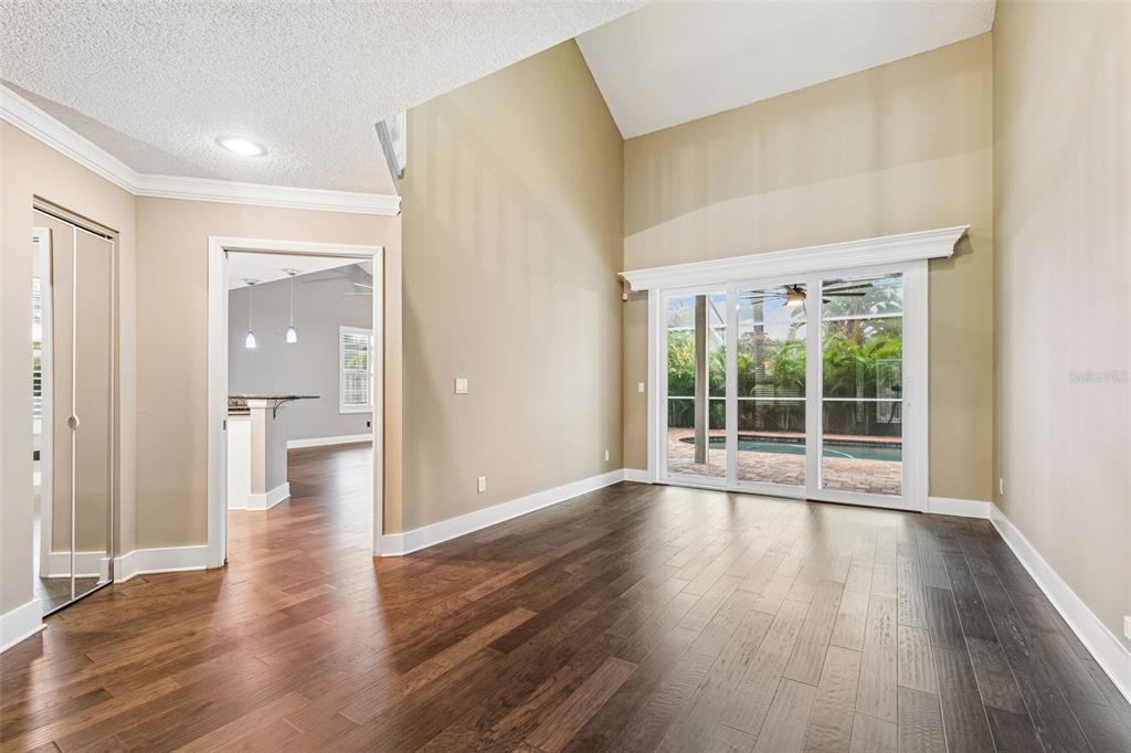 A room with dark wood flooring, vaulted ceilings, and sliding glass doors overlooking a pool — 1128 MAINSAIL DRIVE, TARPON SPRINGS, FL