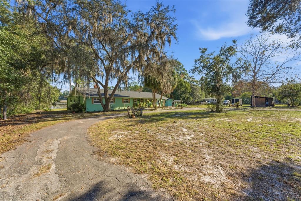 A light green house sits on a large, grassy lot with a paved driveway — 26310 FISHERMANS ROAD, PAISLEY, FL
