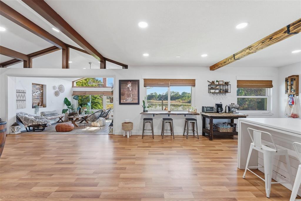 A spacious open-concept room features wood-look flooring, exposed ceiling beams, and a view of a lake — 26310 FISHERMANS ROAD, PAISLEY, FL