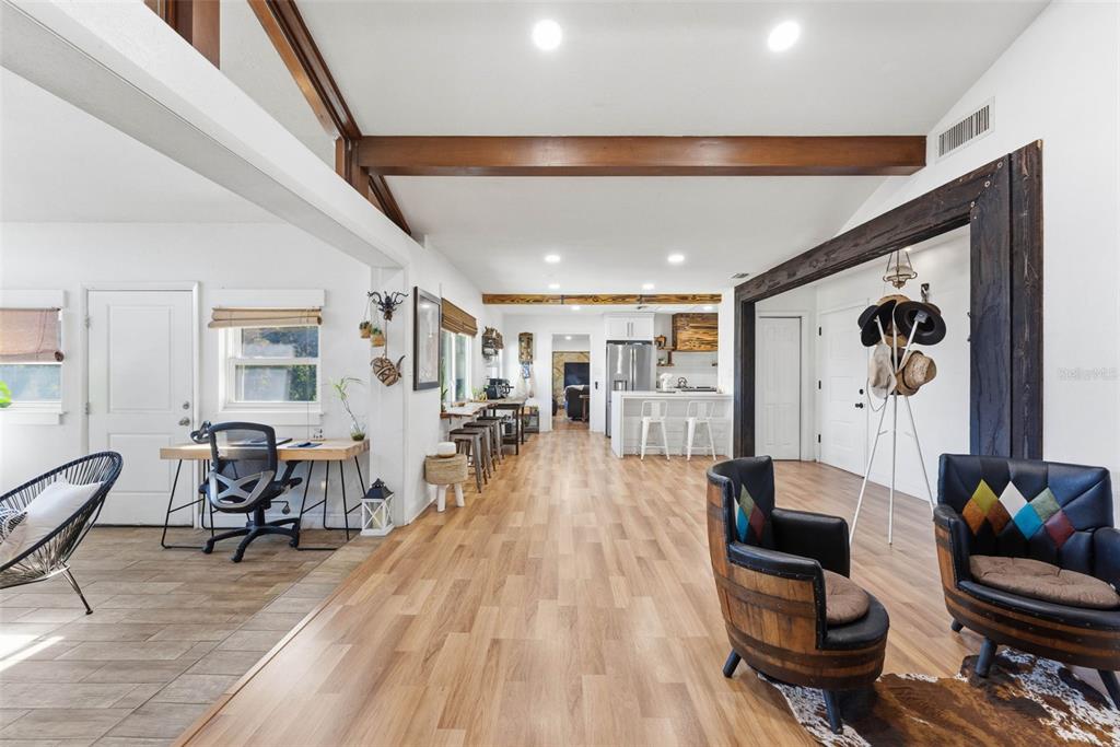 An open-concept living area features wood-look flooring, exposed ceiling beams, and a kitchen in back — 26310 FISHERMANS ROAD, PAISLEY, FL