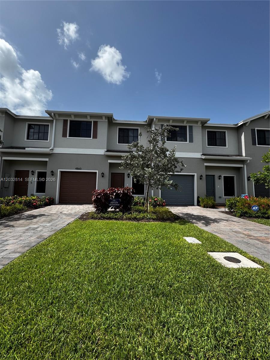 A two-story townhouse exterior features a green lawn, paved driveways, and two garage doors — 4860 Dillion St # 4860, Lake Worth FL 33463, LAKE WORTH, FL