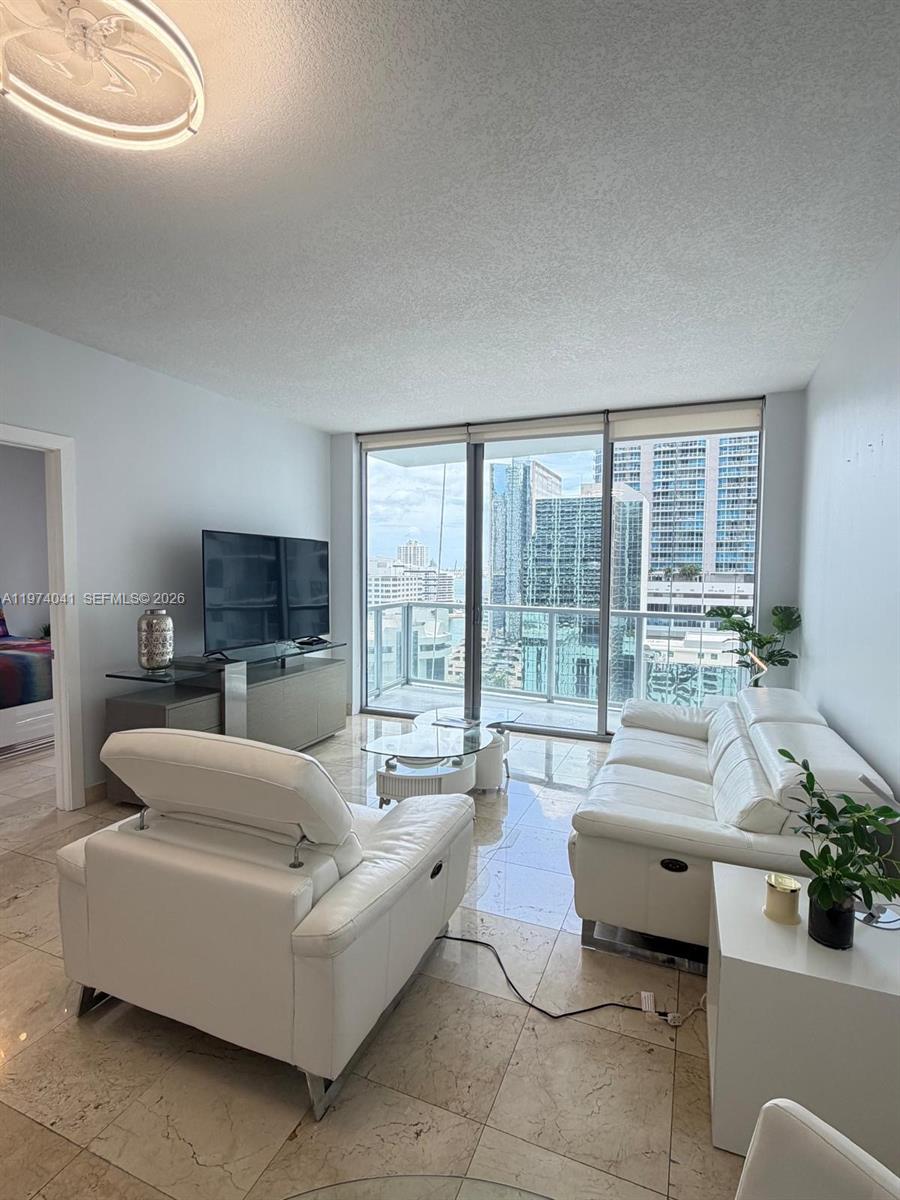 A living room features white leather furniture, tile flooring, and a balcony with city views — 1050 Brickell Ave # 1904, Miami FL 33131, MIAMI, FL