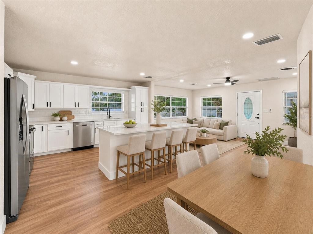 An open-concept kitchen, dining area, and living room featuring white cabinetry, a large island, and wood-look flooring — 5511 CRAIG DRIVE, LAKELAND, FL