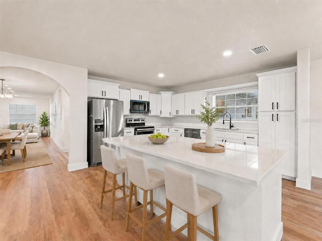 A modern kitchen features white cabinetry, a large quartz island with bar seating, and wood flooring — 5511 CRAIG DRIVE, LAKELAND, FL