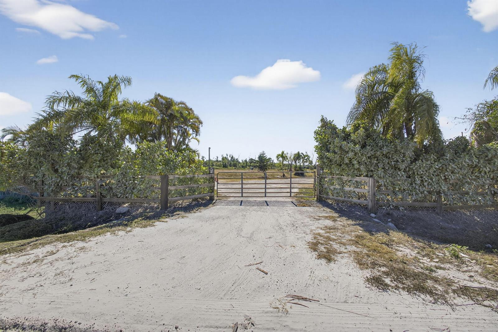 A metal gate sits at the entrance of a sandy driveway flanked by wooden fencing — 16296 Deer Path Lane, Wellington FL 33470, WELLINGTON, FL