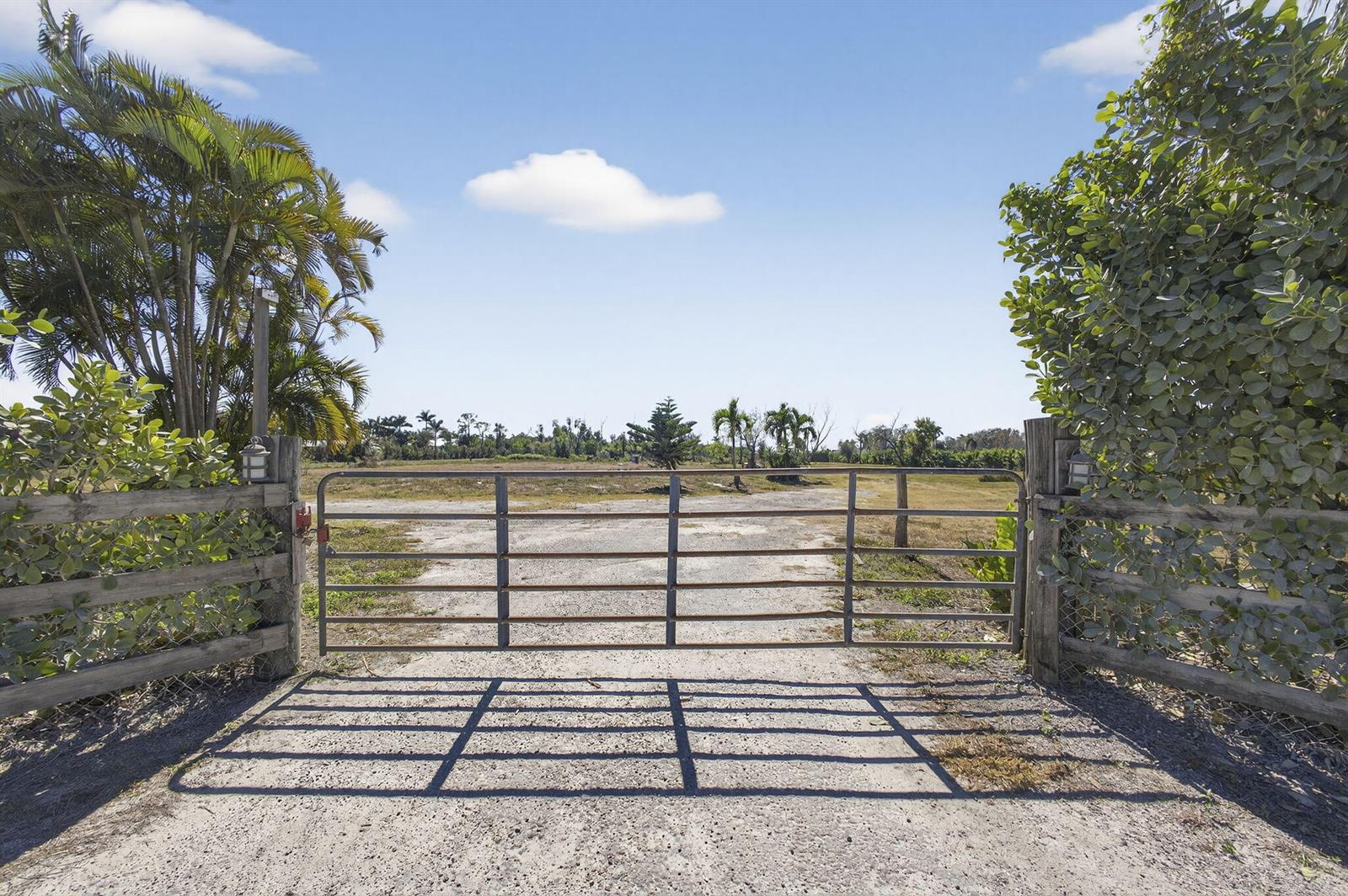 A metal farm gate stands at the entrance to a gravel driveway on a sunny day — 16296 Deer Path Lane, Wellington FL 33470, WELLINGTON, FL