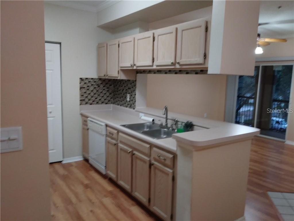A kitchen features light wood cabinets, a laminate countertop, a double sink, and tiled backsplash — 5620 PINNACLE HEIGHTS CIRCLE UNIT 305, TAMPA, FL