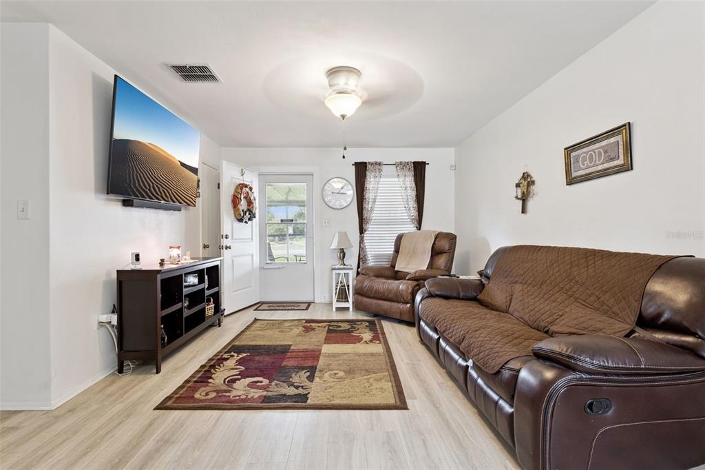 A living room features a brown leather sofa, a recliner, a television, and wood-look flooring — 40522 W 5TH AVENUE, UMATILLA, FL