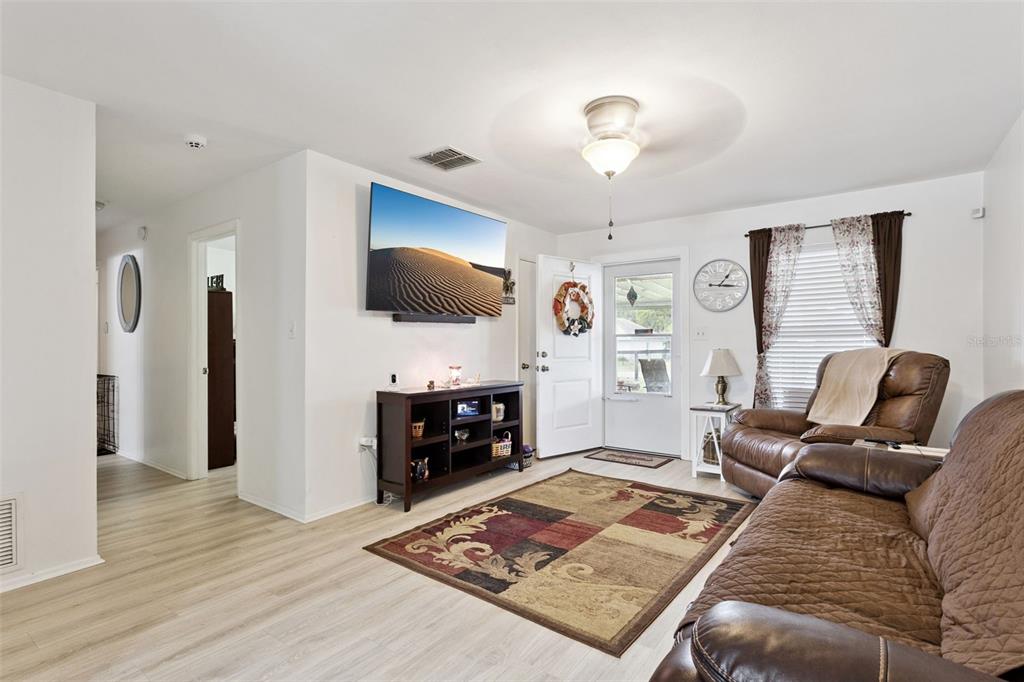 A living room features light wood-look flooring, a wall-mounted television, and brown leather furniture — 40522 W 5TH AVENUE, UMATILLA, FL