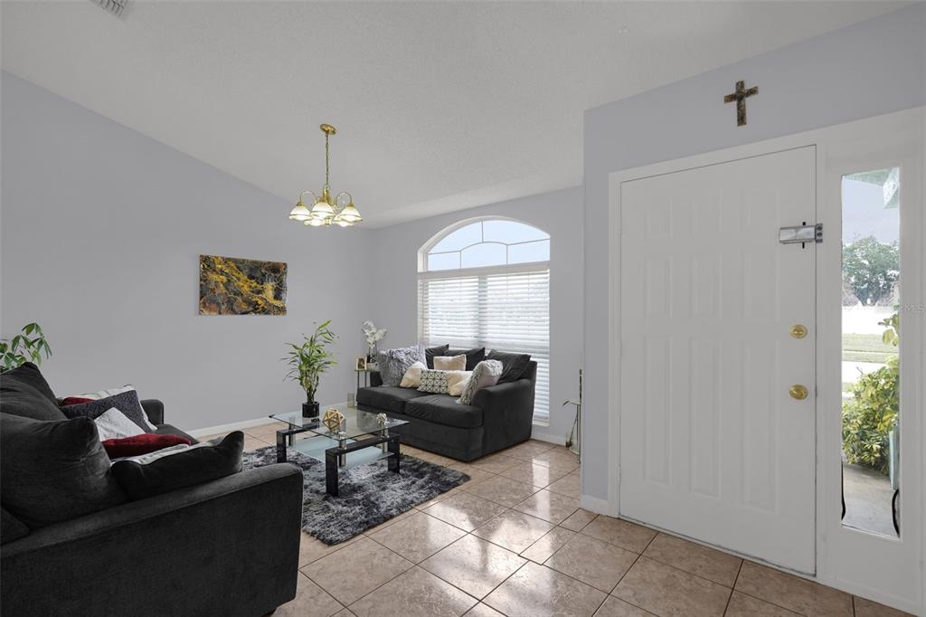 A living room with tile floors, two dark sofas, a glass coffee table, and front door — 230 LYTTON CIRCLE, ORLANDO, FL