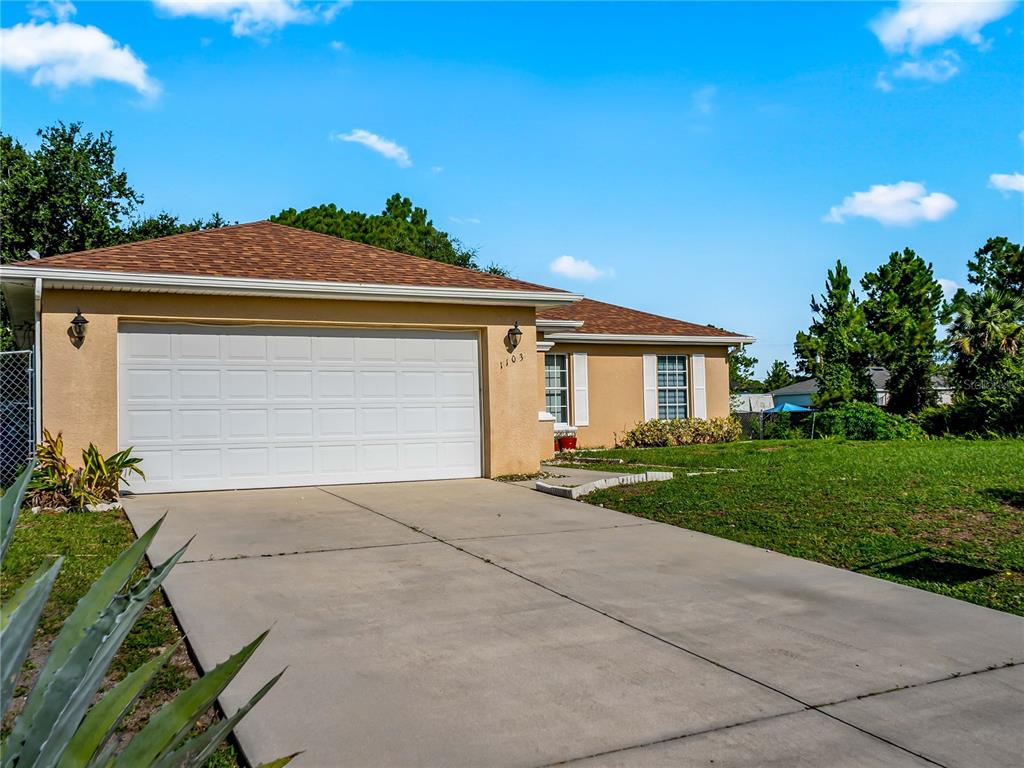 A single-story house with a tan stucco exterior, a two-car garage, and a concrete driveway — 1103 LEE AVENUE, LEHIGH ACRES, FL