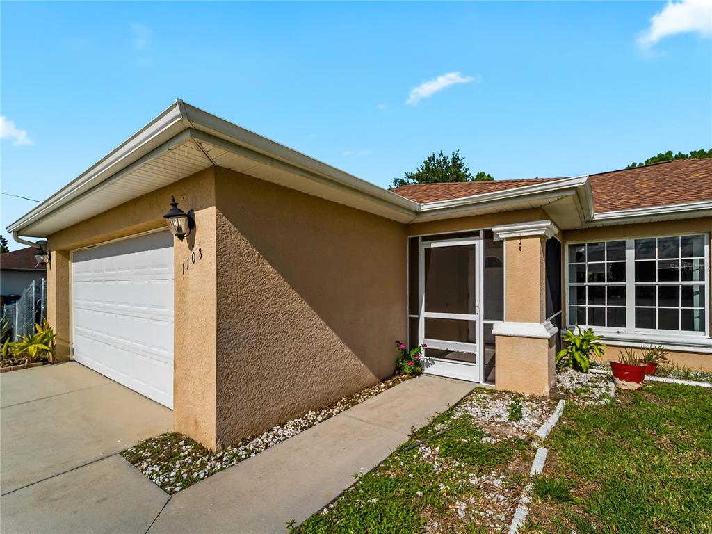 A tan stucco house exterior features a white garage door, a screened entryway, and windows — 1103 LEE AVENUE, LEHIGH ACRES, FL