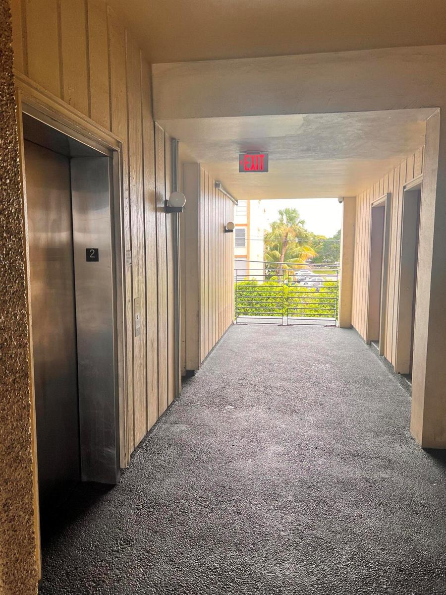 An outdoor apartment hallway features an elevator, wood-paneled walls, and a metal railing — 2331 N State Rd 7 # 207, Lauderhill FL 33313, LAUDERHILL, FL