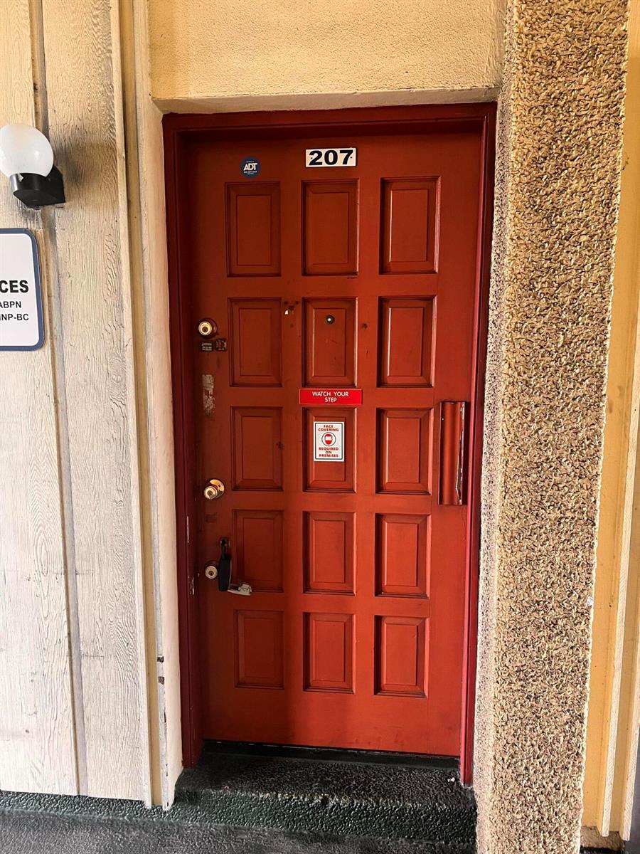 A red door marked 207 features an ADT security sticker and two posted safety signs — 2331 N State Rd 7 # 207, Lauderhill FL 33313, LAUDERHILL, FL