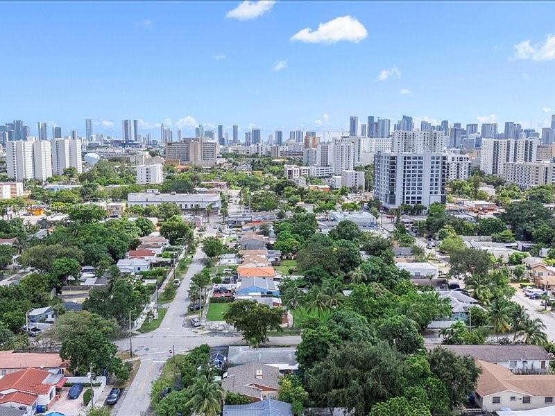 An aerial view shows a residential neighborhood with houses and trees leading toward a city skyline — 1810 NW 16th Ter, Miami FL 33125, MIAMI, FL