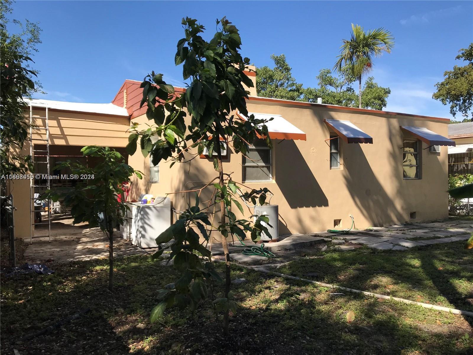 The exterior of a tan house features a covered carport, metal awnings, and young trees — 1810 NW 16th Ter, Miami FL 33125, MIAMI, FL