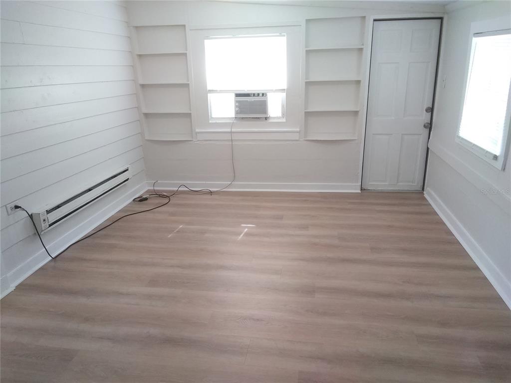 A room with light wood-look flooring, white shiplap walls, built-in shelving, and a window unit — 2609 4TH STREET S UNIT 2, ST PETERSBURG, FL
