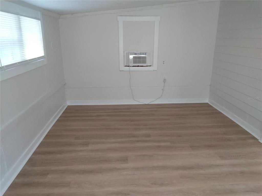 An empty room features light wood-look flooring, white walls, a window, and a wall-mounted air conditioner — 2609 4TH STREET S UNIT 2, ST PETERSBURG, FL