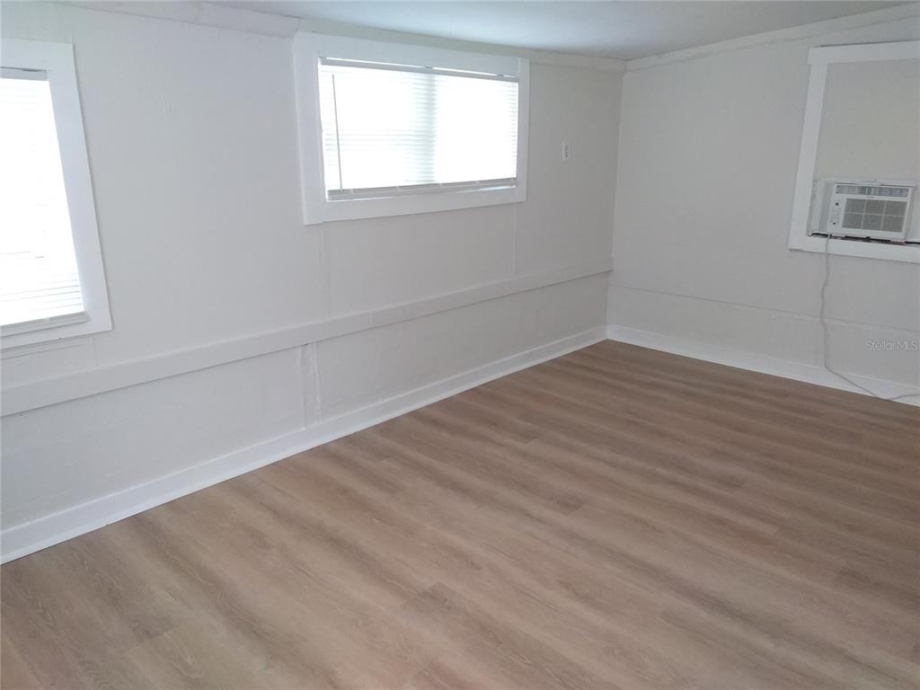 An empty room features light-colored wood-look flooring, white walls, two windows, and a wall-mounted air conditioner — 2609 4TH STREET S UNIT 2, ST PETERSBURG, FL