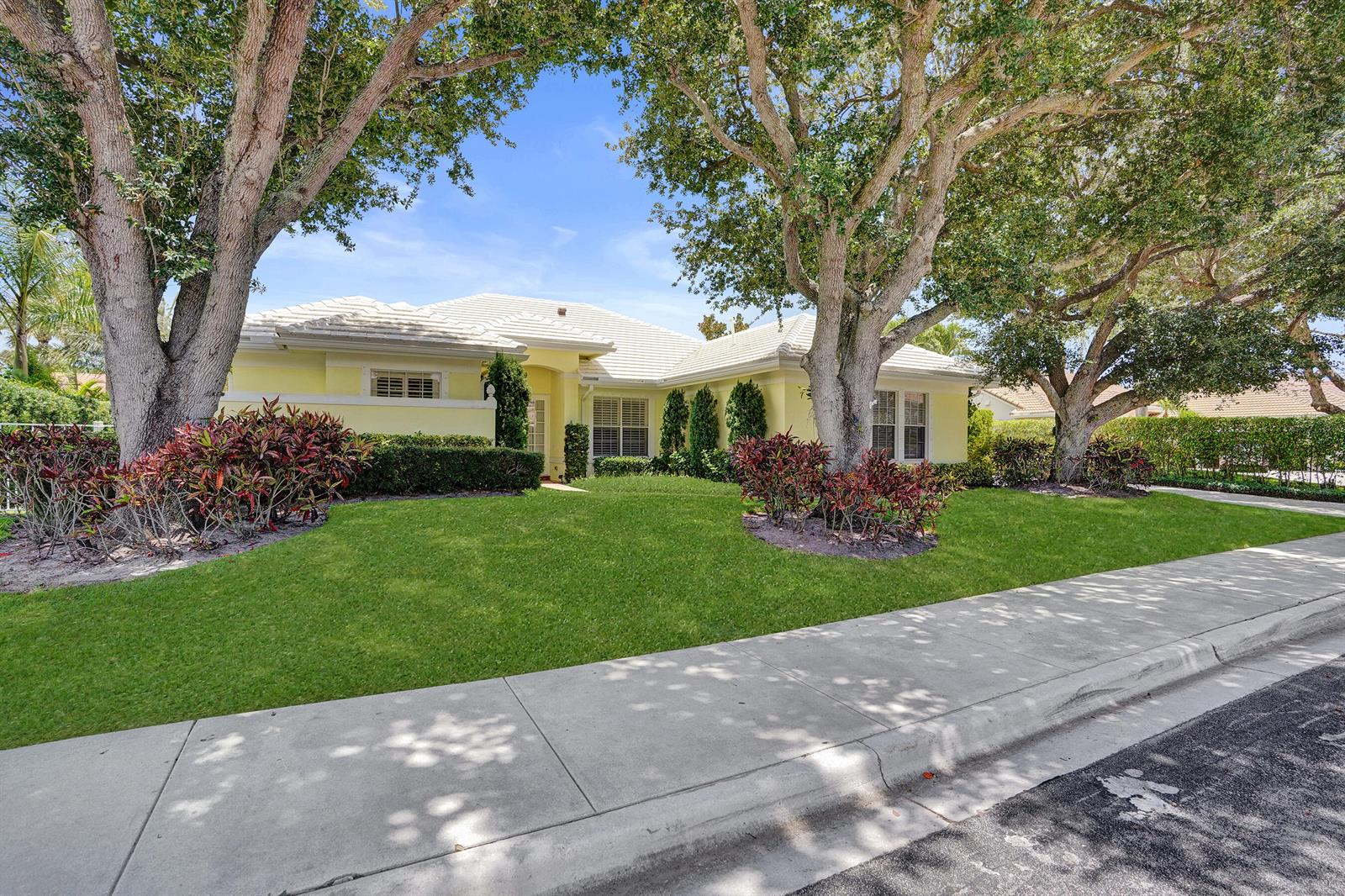 A yellow single-story house with a tiled roof sits behind a lawn and large trees — 2760 Tecumseh Drive, West Palm Beach FL 33409, WEST PALM BEACH, FL
