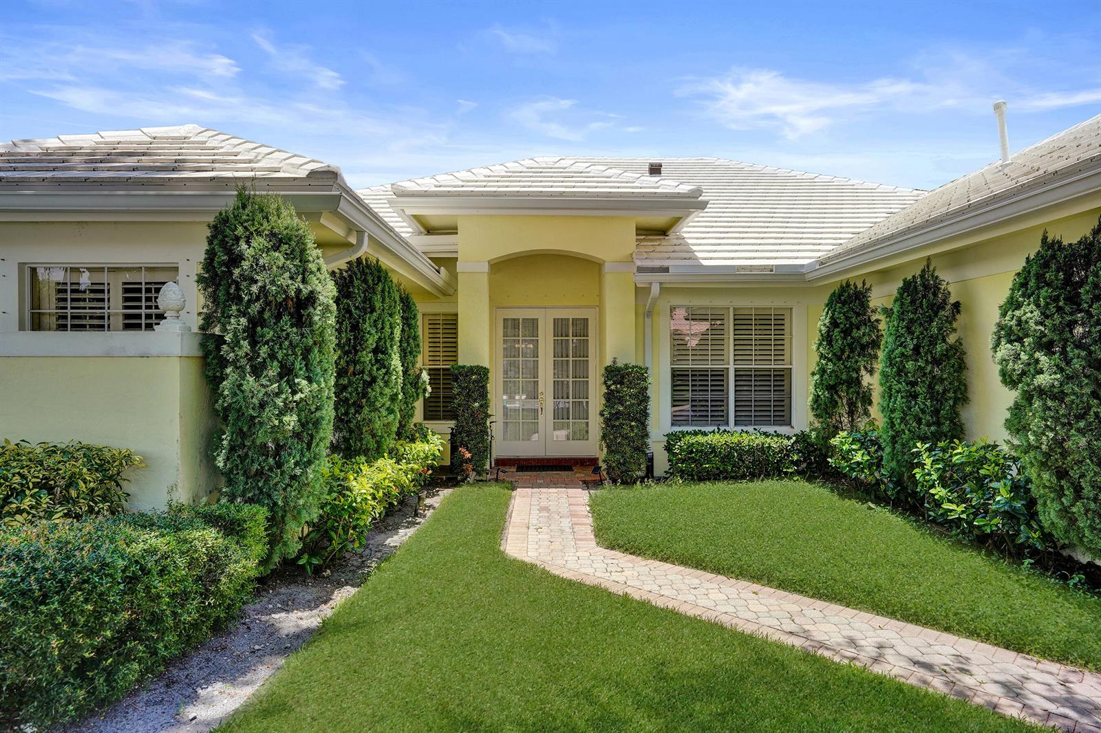 A yellow house with a white tiled roof features a brick walkway leading to double doors — 2760 Tecumseh Drive, West Palm Beach FL 33409, WEST PALM BEACH, FL