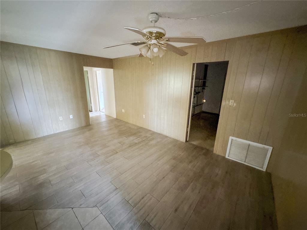 A room with wood-paneled walls, a ceiling fan, and light-colored wood-look tile flooring — 3234 DANTE DRIVE, SARASOTA, FL