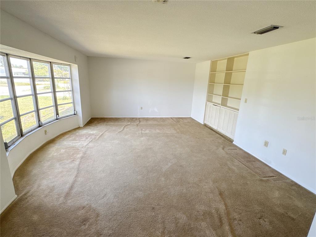 An empty room features beige wall-to-wall carpeting, a large window, and built-in white shelving — 3234 DANTE DRIVE, SARASOTA, FL