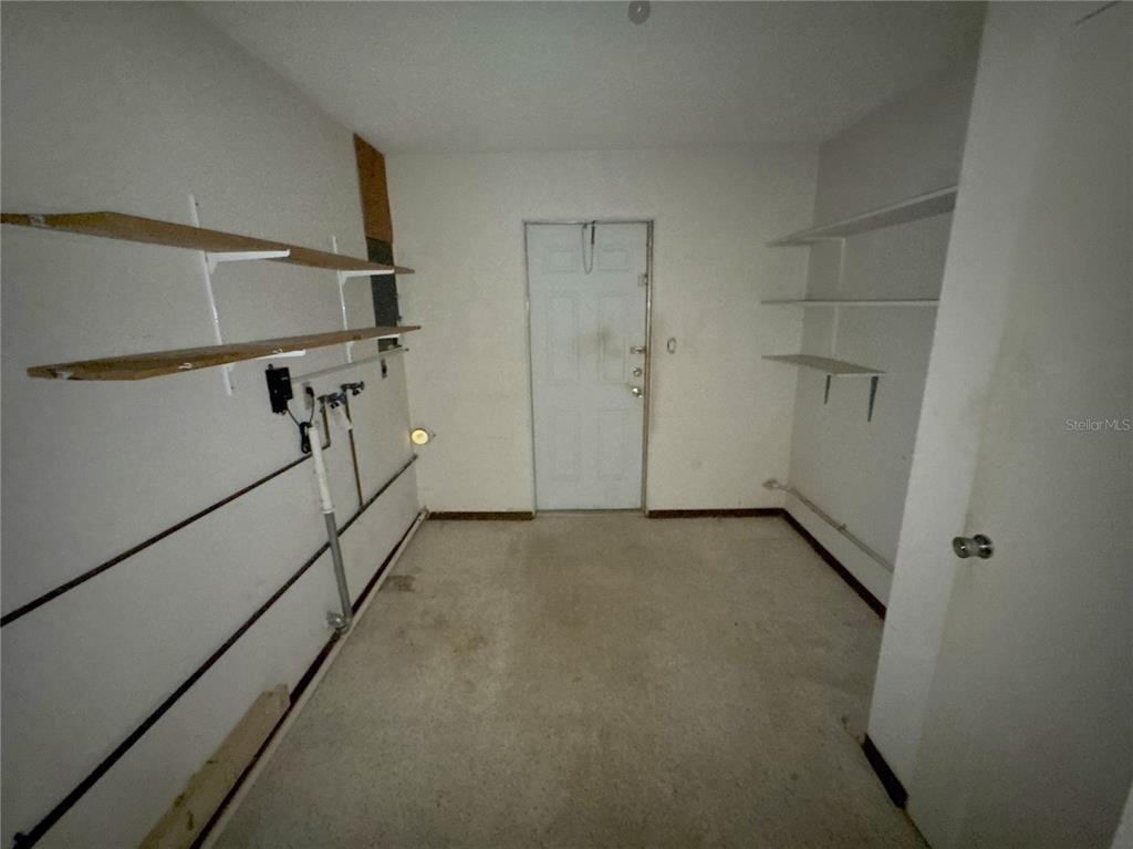 A utility room with concrete floors, white walls, open shelving, and a central exterior door — 3234 DANTE DRIVE, SARASOTA, FL