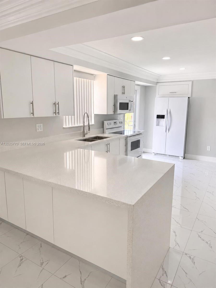A modern kitchen features white cabinets, quartz countertops, and white marble-patterned tile flooring — 5735 Hayes St, Hollywood FL 33021, HOLLYWOOD, FL