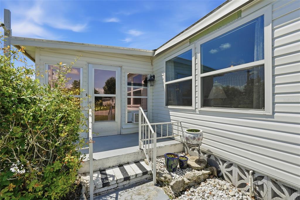 A white mobile home exterior features a small concrete porch, metal railings, and potted plants — 5058 PALENA BOULEVARD, NORTH PORT, FL