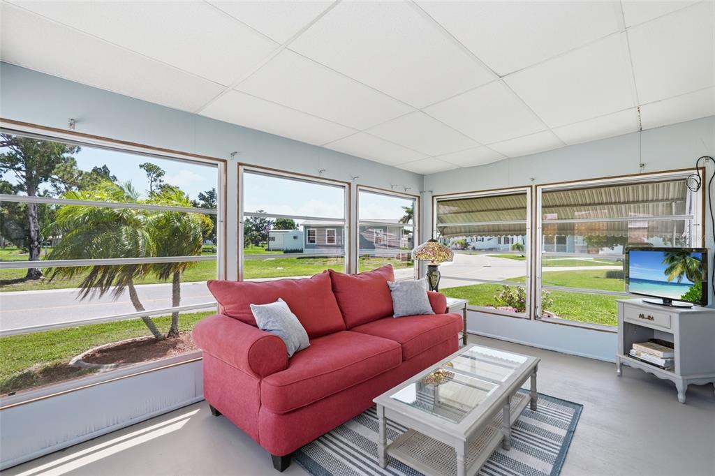 A sunroom features a red sofa, a glass-top coffee table, and large windows overlooking a street — 5058 PALENA BOULEVARD, NORTH PORT, FL