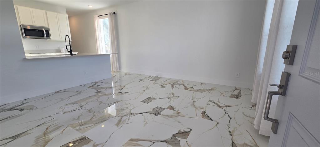 A room with white marble-look tile flooring, white walls, and an open kitchen area — 5560 MORANT BAY PATH, KISSIMMEE, FL