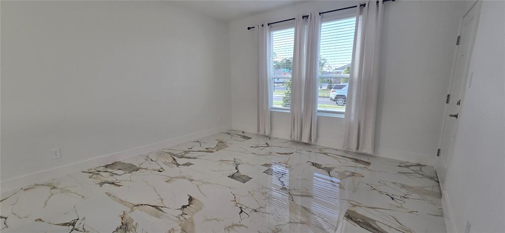An empty room features white walls, large windows with curtains, and polished marble-look tile flooring — 5560 MORANT BAY PATH, KISSIMMEE, FL
